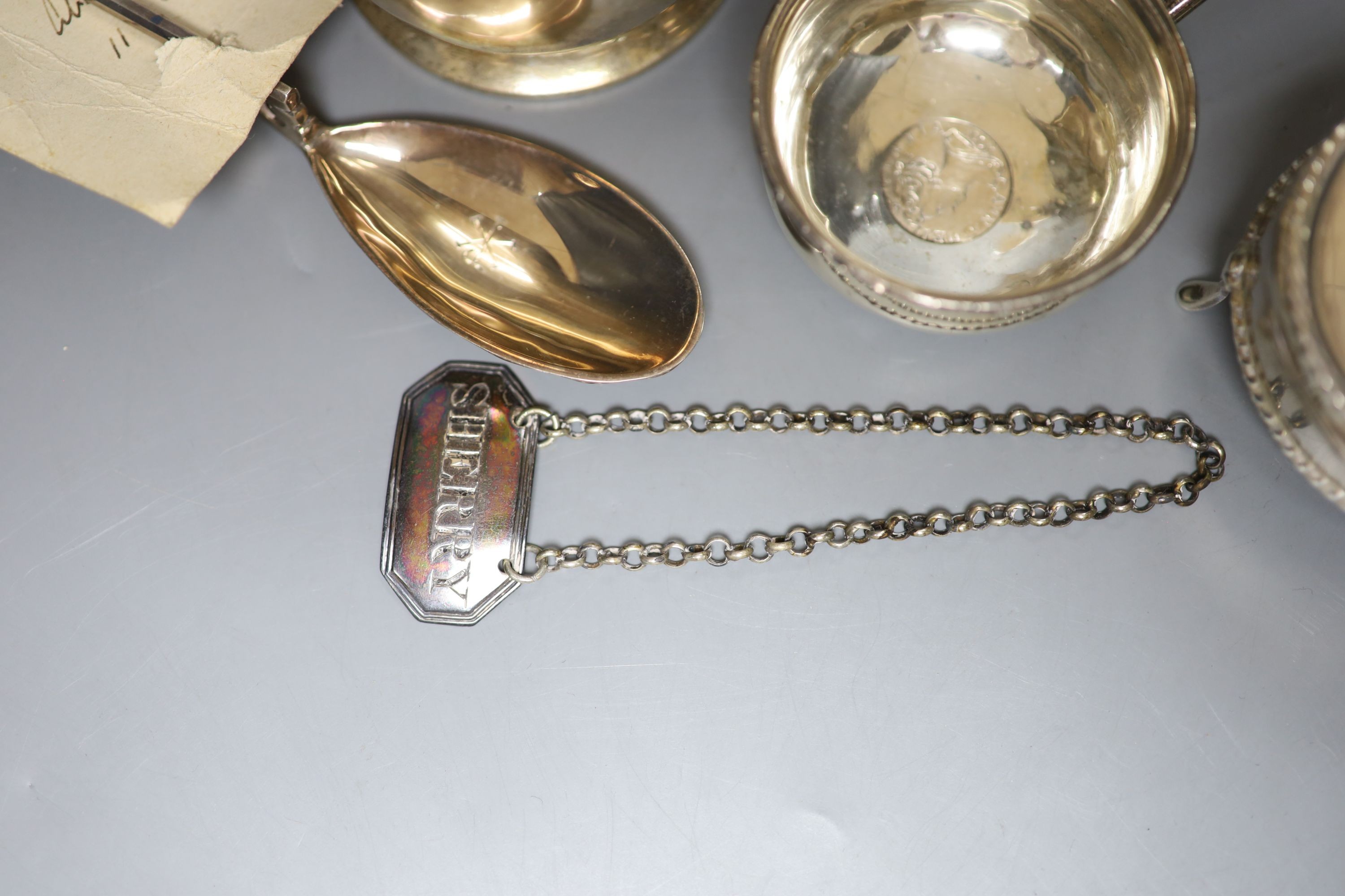 A George V silver mug, a white metal toddy ladle bowl, an Edwardian silver trinket box, a silver reproduction Roman spoon and a George III 'Sherry' label.